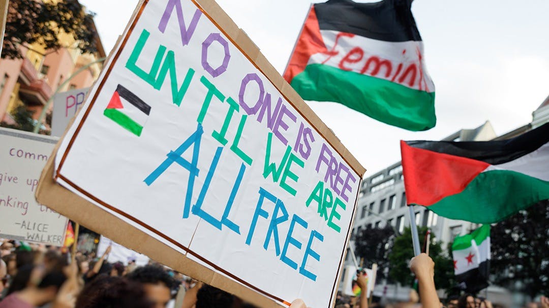 Placards and flags at a pro-Palestine demonstration in Berlin. Placard reads: 'No one is free until we are all free'