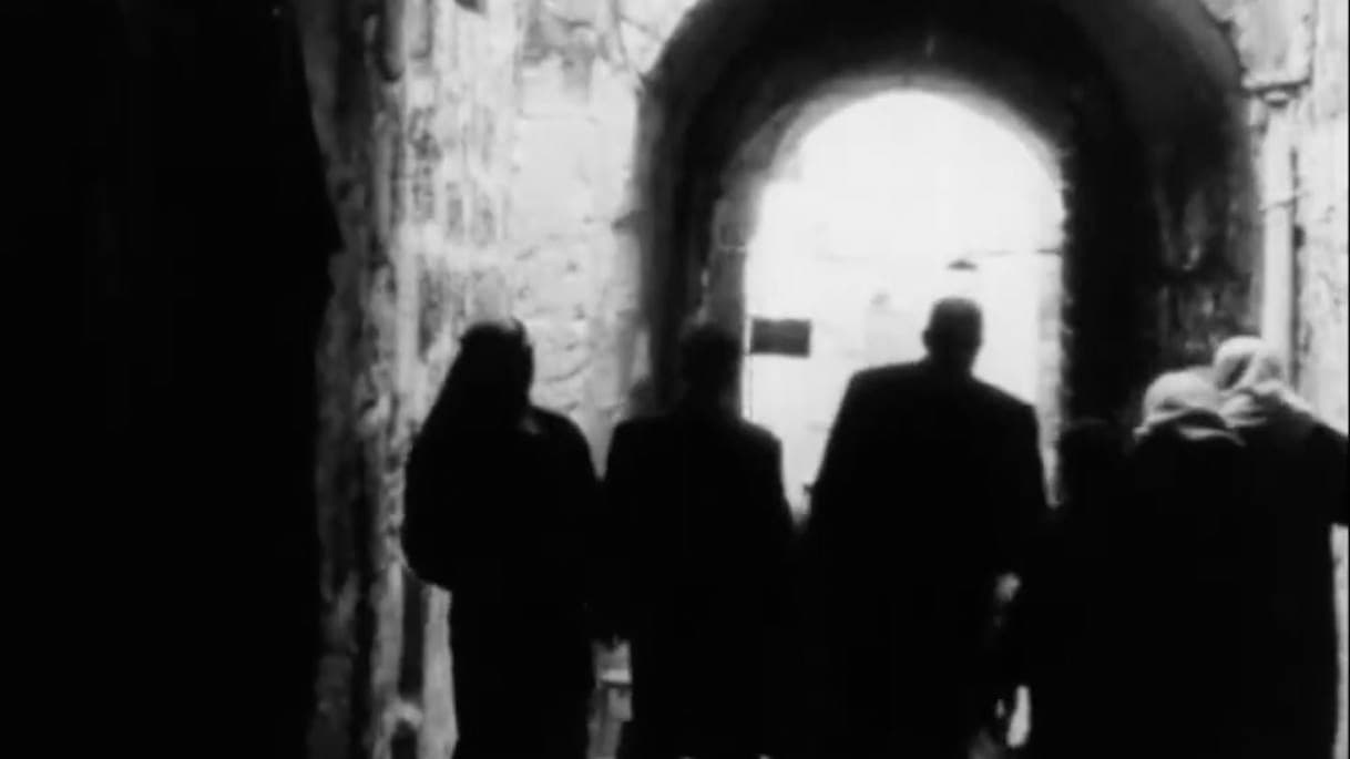 A black and white photo of four women and one man in the middle walking towards an arch.
