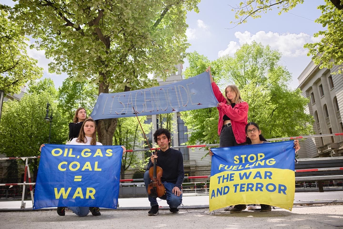 Arshak Makichayan demonstrating with a group of people holding posters that read: 'Oil, gas, coal = war', 'It's a Genocide', and 'stop fuelling the war and terror'